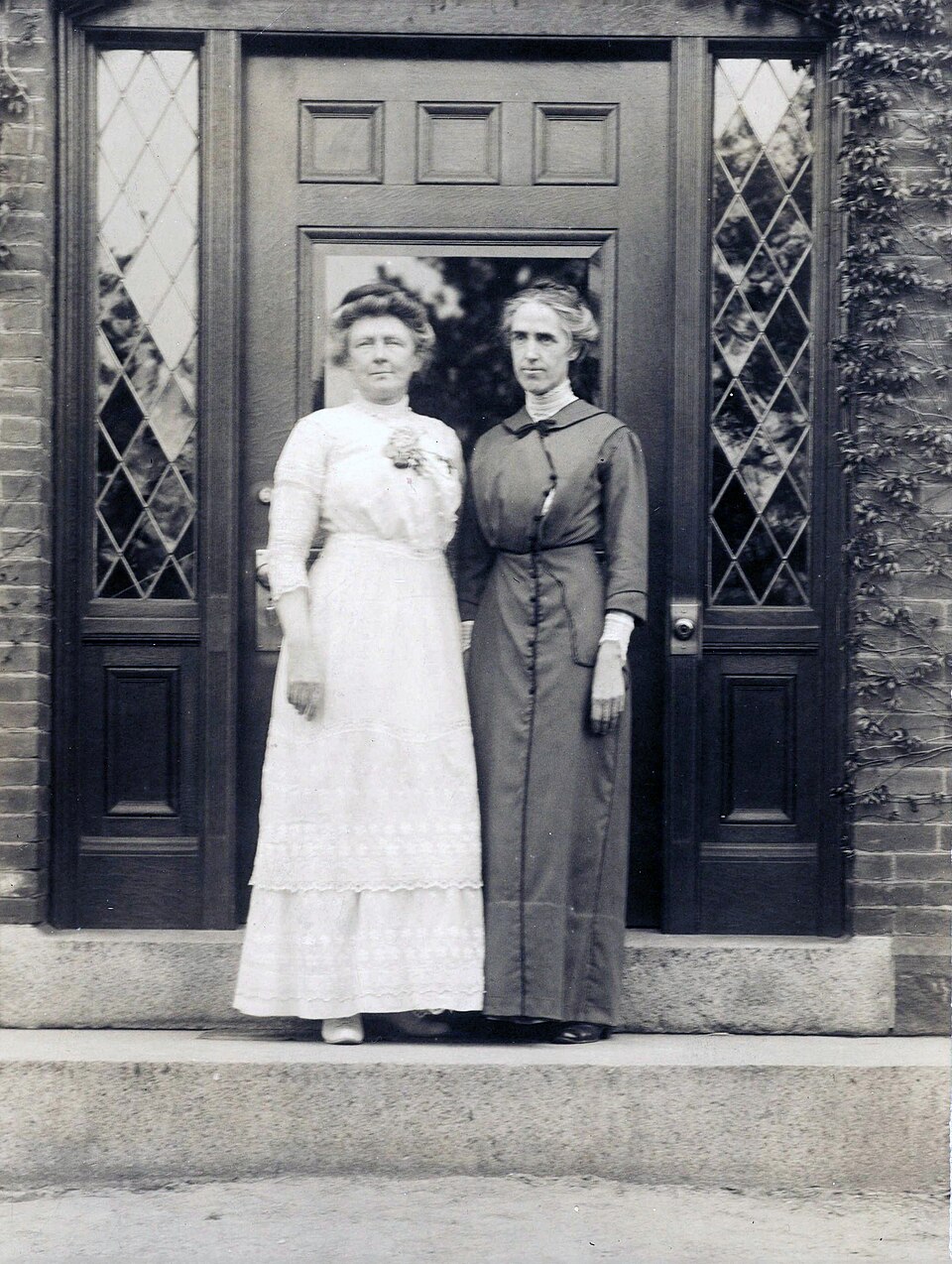 Annie Jump Cannon in a white dress and Henrietta Swan Leavitt in a dark dress standing together in a doorway at the Harvard College Observatory, 1913.