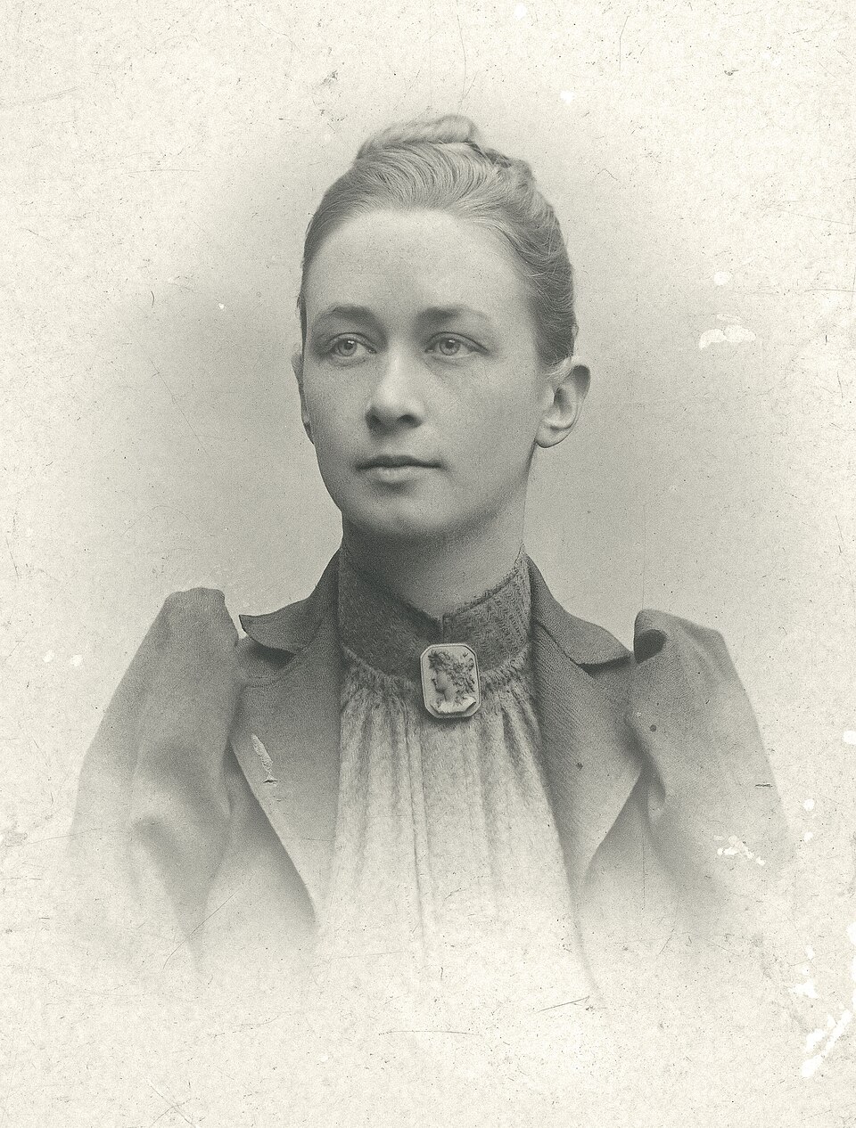 Black and white portrait of Hilma af Klint with her hair pinned up, wearing a jacket and a cameo brooch at the collar.