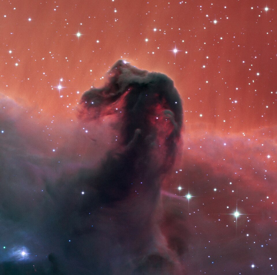 Colour image of the Horsehead Nebula: a dark, distinct horse-head-shaped silhouette of cold dust against a glowing red-orange field of ionized hydrogen gas, scattered with bright stars.