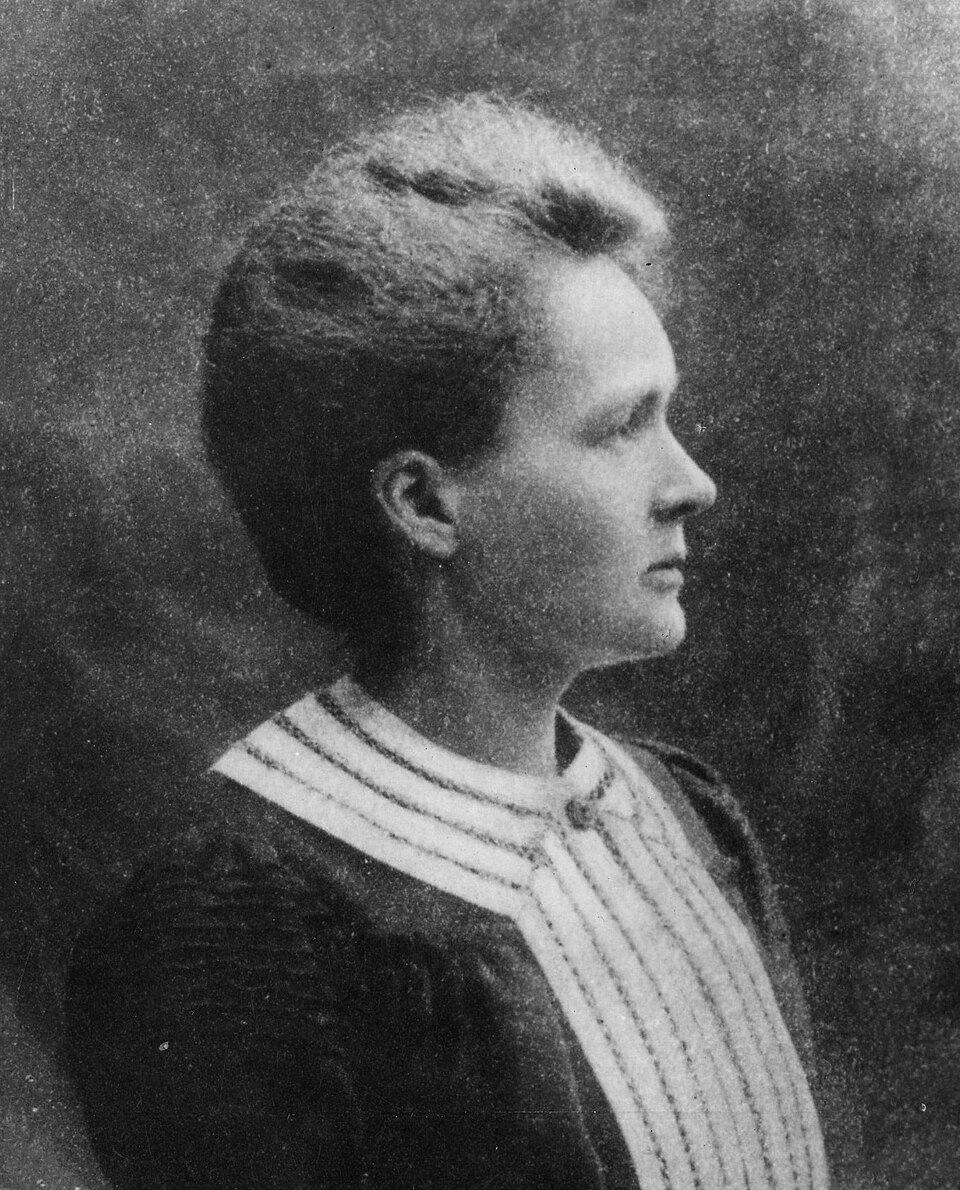Black and white profile portrait of Marie Curie, c. 1903, in a dark dress with a striped collar.